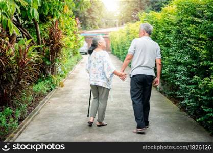 Happy senior couple walking together in the garden. Old elderly using a walking stick to help walk balance. Concept of Love and care of the family And health insurance for family