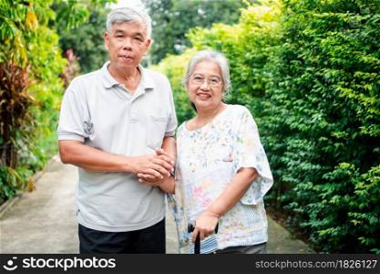 Happy senior couple walking together in the garden. Old elderly using a walking stick to help walk balance. Concept of Love and care of the family And health insurance for family