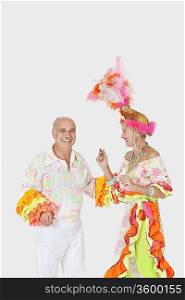 Happy senior dancing couple in Brazilian outfits dancing over gray background