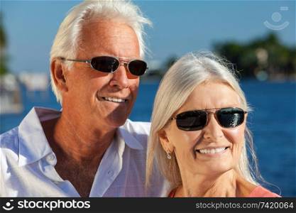 Happy senior loving man and woman romantic couple together outside in sunshine laughing wearing sunglasses by the sea or a river