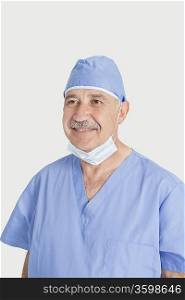 Happy senior male surgeon with surgical mask and cap over gray background