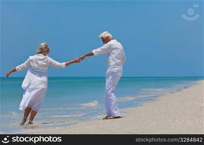 Happy senior man and woman couple dancing and holding hands on a deserted tropical beach with bright clear blue sky