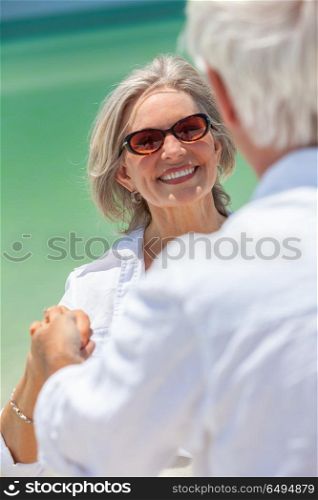 Happy senior man and woman couple dancing and holding hands on a deserted tropical beach with turquoise sea and clear blue sky. Happy Senior Couple Dancing Holding Hands on A Tropical Beach