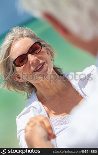 Happy senior man and woman couple dancing and holding hands on a deserted tropical beach with turquoise sea and clear blue sky. Happy Senior Couple Dancing Holding Hands on A Tropical Beach
