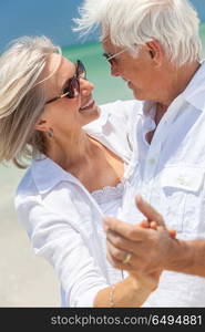 Happy senior man and woman couple dancing and holding hands on a deserted tropical beach with turquoise sea and clear blue sky. Happy Senior Couple Dancing Holding Hands on A Tropical Beach