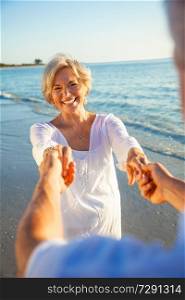 Happy senior man and woman couple dancing and holding hands on a deserted tropical beach at sunset with bright clear blue sky
