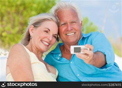 Happy senior man and woman couple laughing and taking photographs with a cell phone on a tropical beach with bright clear blue sky