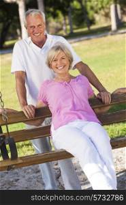 Happy senior man and woman couple sitting together outside in sunshine on a park bench