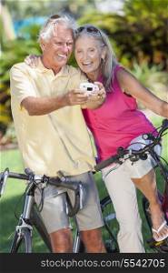 Happy senior man and woman couple together cycling on bicycles taking self portrait picture photograph with digital camera in a sunny green park