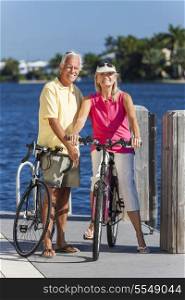 Happy senior man and woman couple together cycling on bicycles with bright clear blue sky by a river or sea