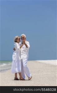 Happy senior man and woman couple together dancing by the sea on a deserted tropical beach with bright clear blue sky