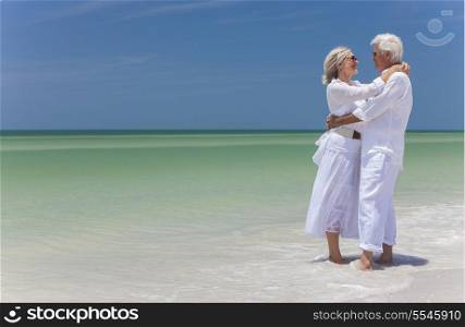 Happy senior man and woman couple together embracing by sea on a deserted tropical beach with bright clear blue sky