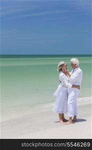Happy senior man and woman couple together embracing by sea on a deserted tropical beach with bright clear blue sky
