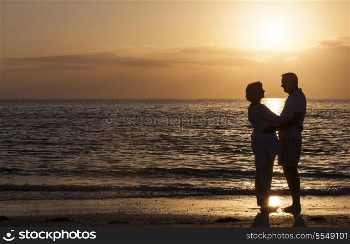 Happy senior man and woman couple together hugging embracing at sunset on a deserted tropical beach