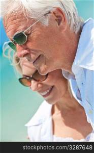 Happy senior man and woman couple together looking out to sea on a deserted tropical beach