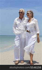Happy senior man and woman couple together looking out to sea on a deserted tropical beach with bright clear blue sky.