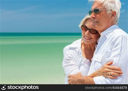 Happy senior man and woman retired couple embracing wearing sunglasses on a deserted tropical beach with turquoise sea and clear blue sky. Happy Senior Couple Dancing Embracing on a Tropical Beach