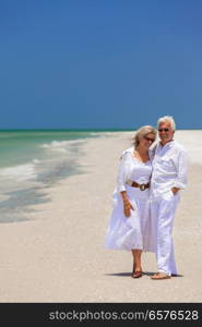 Happy senior man and woman retired couple laughing and embracing wearing sunglasses on a deserted tropical beach with turquoise sea and clear blue sky
