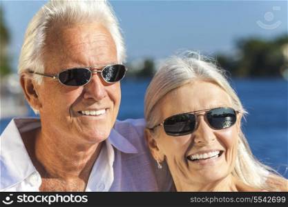 Happy senior man and woman romantic couple together looking out to tropical sea or river wearing sunglasses