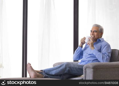 Happy senior man having coffee while relaxing on sofa at home