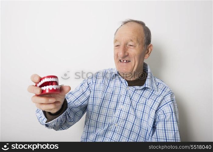 Happy senior man holding dentures against gray background