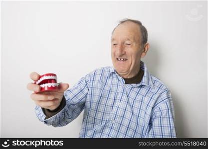 Happy senior man holding dentures against gray background