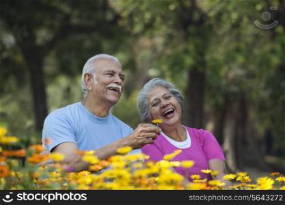 Happy senior man smiling with woman at park holding flower