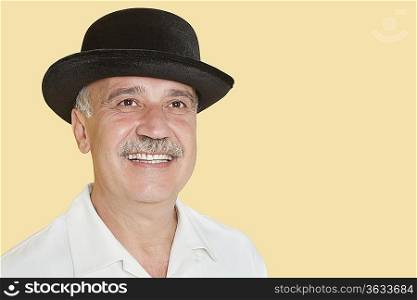 Happy senior man wearing hat while looking up over yellow background