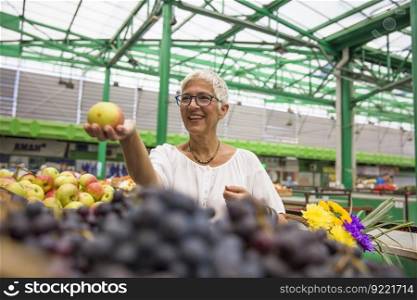 Happy senior woman buying apples on market