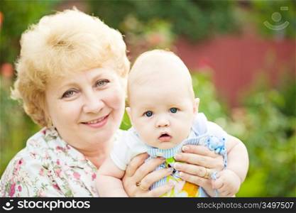 Happy senior woman holding baby boy in spring flowery garden. Nature green blurred background