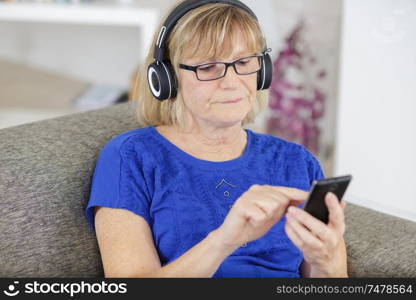 happy senior woman in headphones and smartphone at home