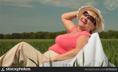 Happy senior woman relaxing on a green meadow, looking at the camera, smiling