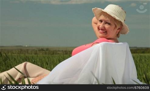 Happy senior woman relaxing on a green summer field