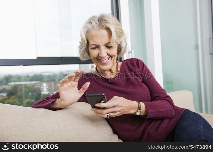 Happy senior woman text messaging through smart phone on sofa at home