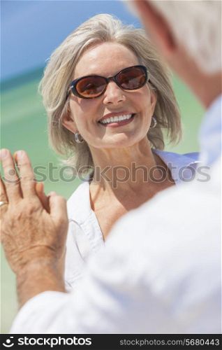 Happy senior woman with perfect teeth dancing with man in a couple and holding hands on a deserted tropical beach with bright clear blue sky