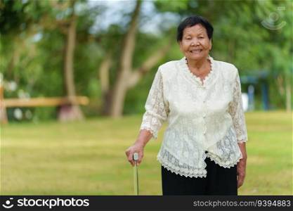 happy senior woman with walking stick in the grass field at the park