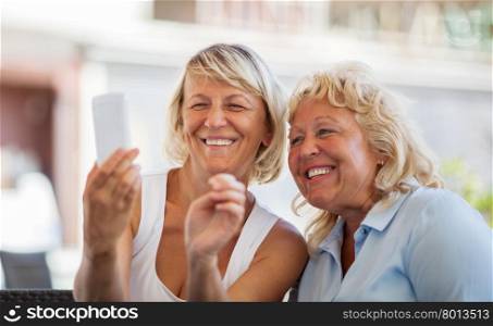 Happy senior women friends taking phone selfie or looking at made shots and smiling. Modern mature women making happy mobile selfie