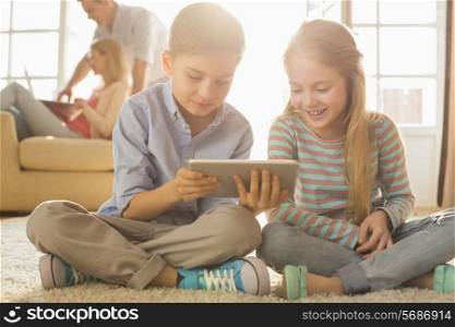 Happy siblings using digital tablet on floor with parents in background