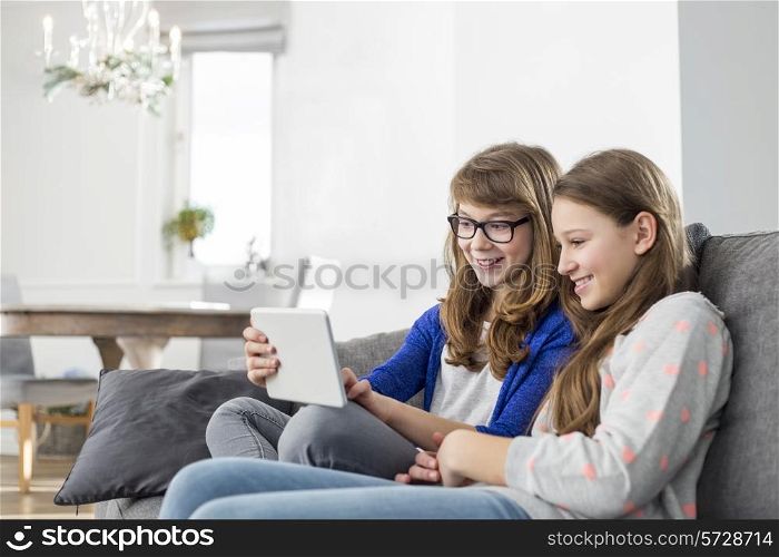 Happy sisters using digital tablet on sofa at home