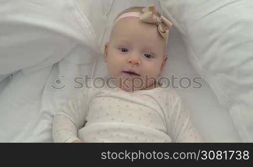 Happy six months baby girl on the bed. Lovely blue-eyed child with a bow