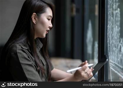 happy smile freelance asian people business female casual working taking note on digital tablet with electronic pen wearing brownish green dress stylish hipster Summer in coffee shop Cafe background