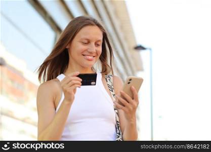 Happy smile young adult woman consumer using credit card and smartphone. people shopping via online application media concept. big shopping mall on summer day background with copy space.. Happy smile young adult woman consumer using credit card and smartphone. people shopping via online application media concept. big shopping mall on summer day background with copy space