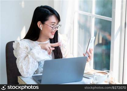 Happy smiley face asian freelance people Businesswoman wearing wireless earphones using smartphone video call camera and talking while casual working with laptop computer at the cafe,Lifestyle