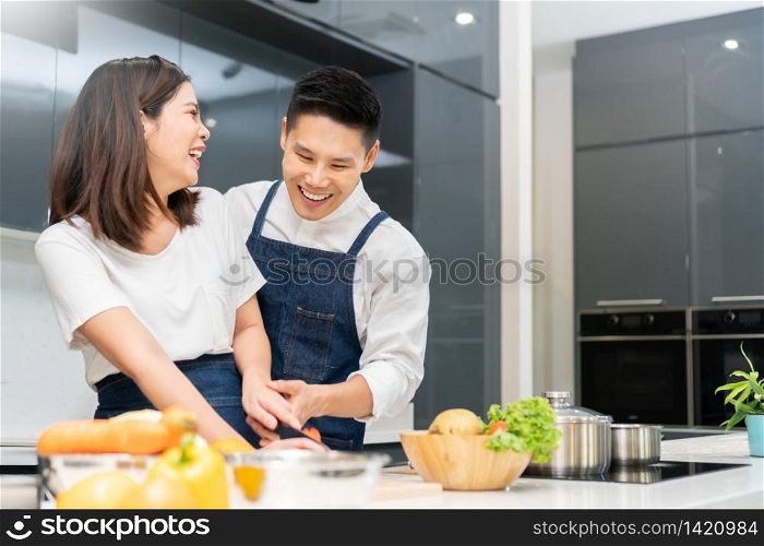 Happy Smiling Asian couple cooking in the kitchen at home. Young Man and beautiful woman in white clothes having fun preparing vegetable for salad.