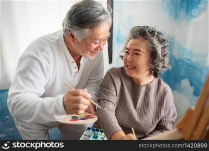 Happy smiling Asian Elderly Couple oil painting on canvas at house. Artist Senior man and woman in sweaters and holding paintbrush, palette after Retirement. Art, Watercolor and Acrylic color.