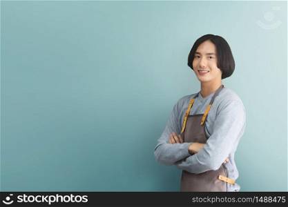Happy smiling Asian man Barista in brown apron with arms crossed looking to camera and standing over blue or green background. copy space. Business Owner.