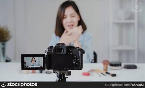 Happy smiling asian woman or beauty blogger with brush and camera recording video and waving hand at home. Beauty videoblog blogging people concept.