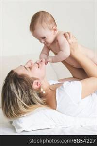 Happy smiling baby boy playing with young mother on bed