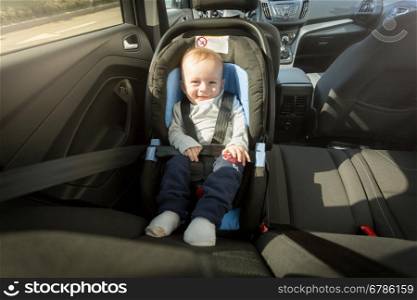 Happy smiling baby boy posing in child safety car seat