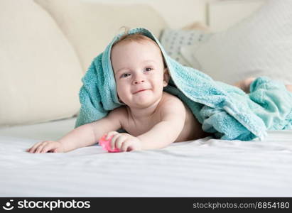 Happy smiling baby under blue towel crawling on bed with white sheets